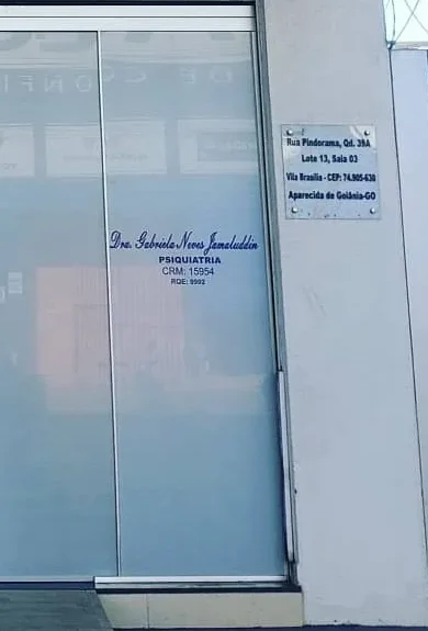 Porta de vidro do consultório com o nome Dra. Gabriela Neves Jamaluddin, Psiquiatria, e a placa do endereço na parede ao lado
